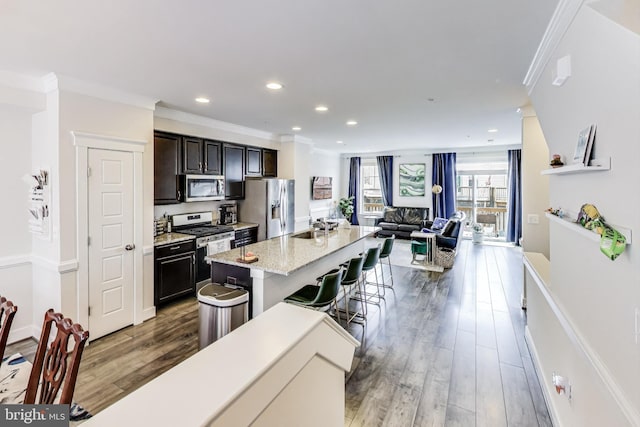 kitchen featuring a kitchen bar, hardwood / wood-style floors, a center island with sink, crown molding, and appliances with stainless steel finishes