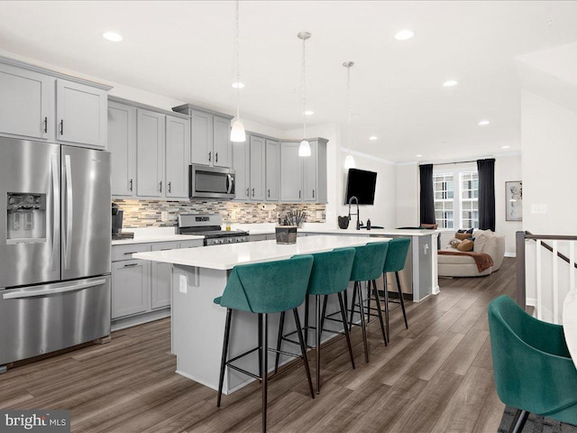 kitchen with stainless steel appliances, dark wood-type flooring, decorative light fixtures, gray cabinets, and a breakfast bar