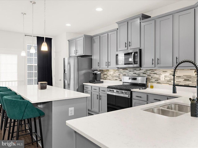 kitchen featuring gray cabinetry, a kitchen breakfast bar, sink, decorative backsplash, and stainless steel appliances