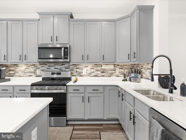 kitchen with backsplash, gray cabinets, sink, and appliances with stainless steel finishes