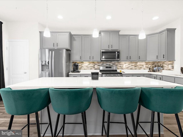 kitchen with a kitchen bar, stainless steel appliances, a kitchen island, and hanging light fixtures