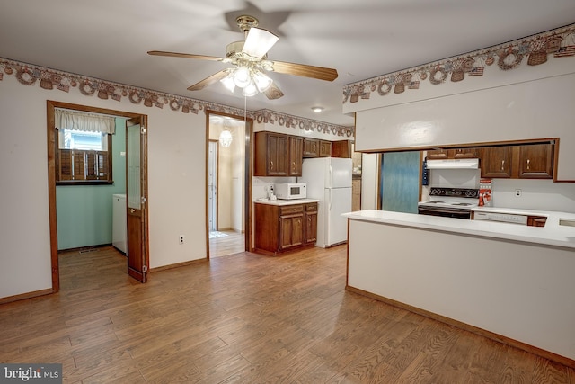 kitchen featuring white appliances, light wood-style flooring, under cabinet range hood, and light countertops