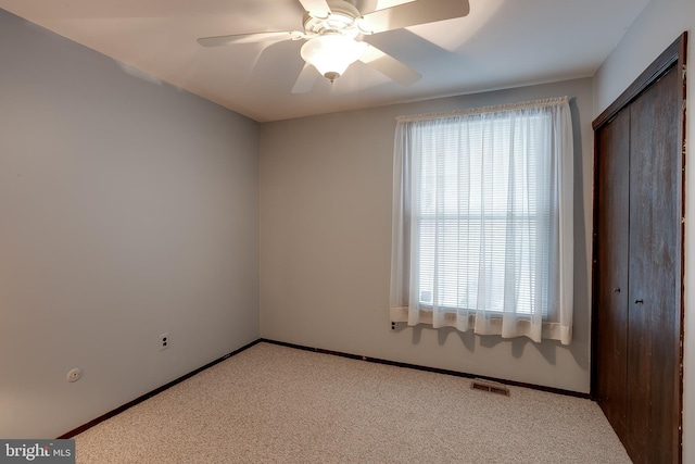 empty room featuring ceiling fan, light colored carpet, visible vents, and baseboards