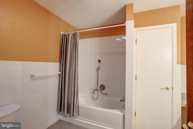 bathroom with toilet, shower / tub combo, a wainscoted wall, and tile walls