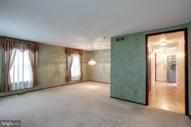 carpeted spare room featuring visible vents and a chandelier