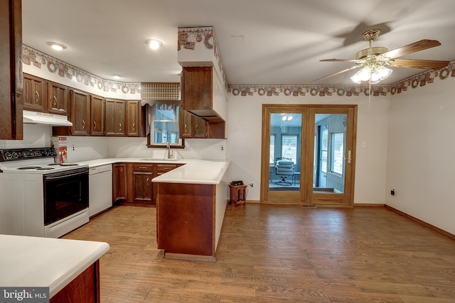 kitchen featuring white appliances, light wood finished floors, a peninsula, light countertops, and under cabinet range hood