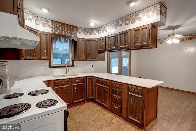 kitchen with light wood-style flooring, a peninsula, light countertops, under cabinet range hood, and a sink