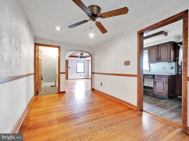 unfurnished room featuring baseboard heating, ceiling fan, a textured ceiling, and light wood-type flooring