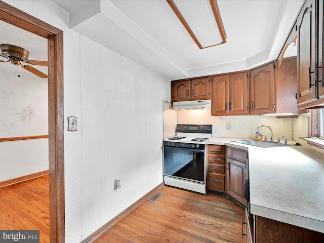 kitchen with hardwood / wood-style floors, ceiling fan, white gas stove, and sink