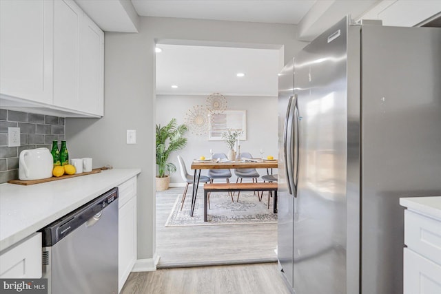 kitchen featuring white cabinets, appliances with stainless steel finishes, light wood-type flooring, and decorative backsplash