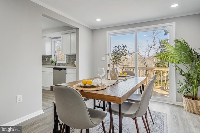 dining room featuring light wood-type flooring, plenty of natural light, ornamental molding, and sink