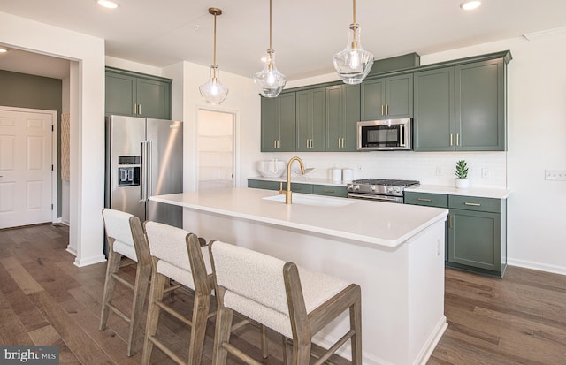 kitchen featuring appliances with stainless steel finishes, dark wood-type flooring, sink, a center island with sink, and hanging light fixtures