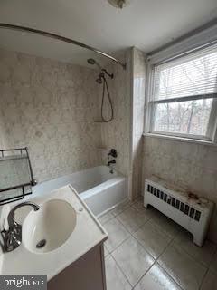 bathroom featuring radiator, sink, tiled shower / bath combo, and tile patterned flooring