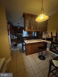 interior space featuring a breakfast bar area, kitchen peninsula, light tile patterned floors, and hanging light fixtures