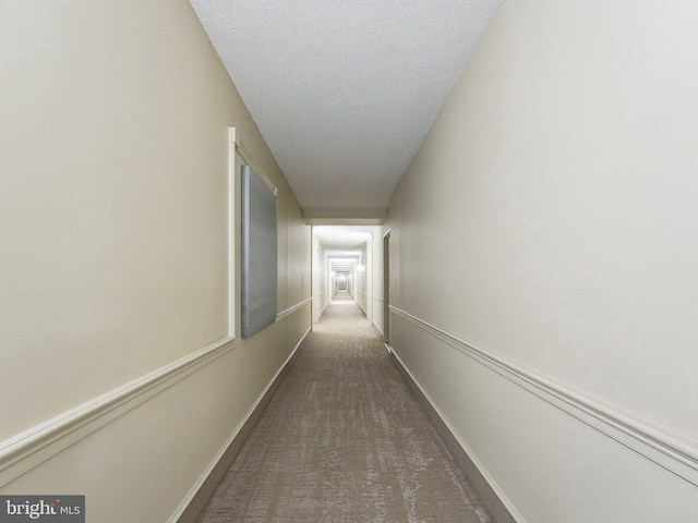 corridor featuring dark carpet and a textured ceiling