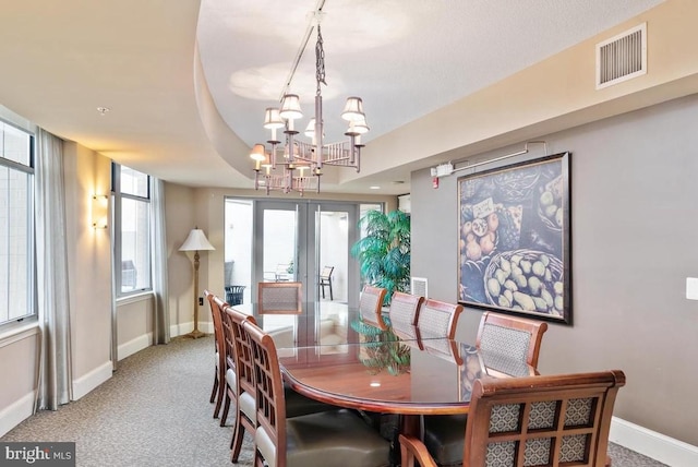 carpeted dining room with french doors, a tray ceiling, and a chandelier