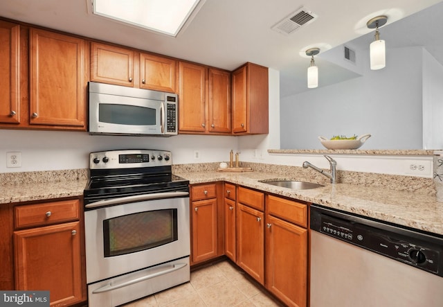 kitchen with sink, light tile patterned floors, appliances with stainless steel finishes, decorative light fixtures, and light stone counters