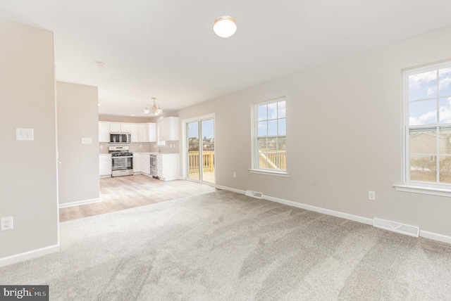 unfurnished living room featuring light carpet and a notable chandelier