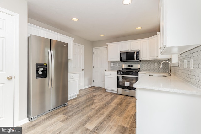 kitchen with light stone countertops, white cabinetry, stainless steel appliances, light hardwood / wood-style floors, and sink