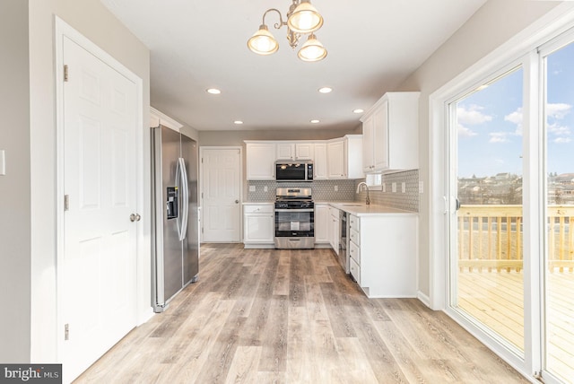 kitchen with light hardwood / wood-style floors, appliances with stainless steel finishes, decorative backsplash, white cabinets, and sink