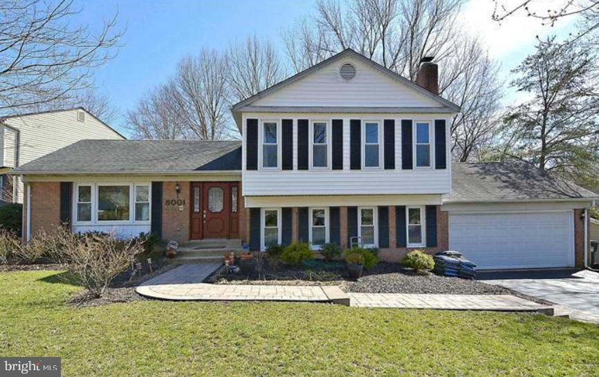 split level home featuring a front yard, concrete driveway, a garage, and a chimney