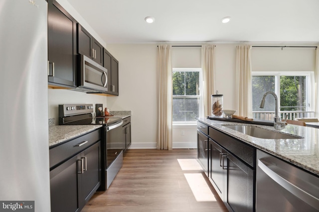 kitchen with sink, stainless steel appliances, light stone counters, light hardwood / wood-style flooring, and dark brown cabinets