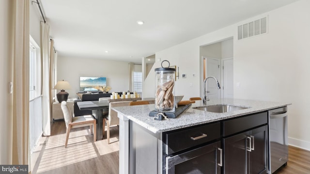 kitchen featuring light stone countertops, sink, stainless steel dishwasher, a center island with sink, and light wood-type flooring