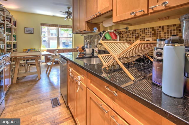 kitchen featuring backsplash, dark stone counters, sink, dishwasher, and light hardwood / wood-style floors