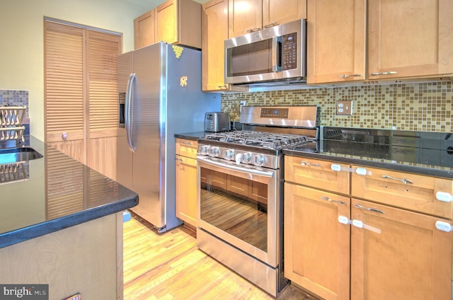 kitchen with backsplash, light hardwood / wood-style floors, stainless steel appliances, and dark stone counters