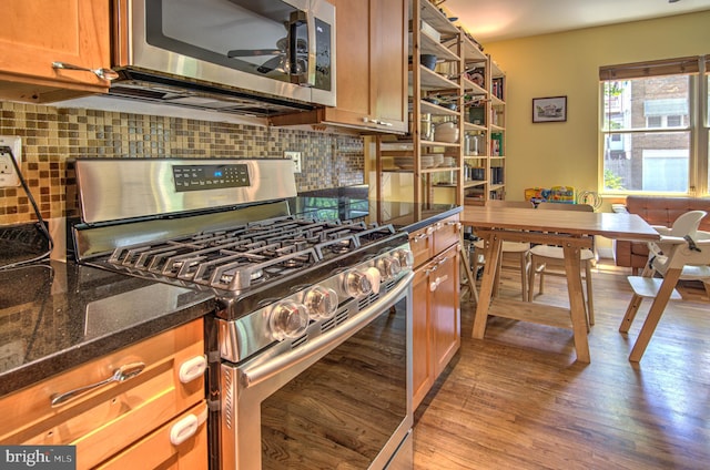 kitchen featuring appliances with stainless steel finishes, backsplash, ceiling fan, dark stone countertops, and light hardwood / wood-style floors