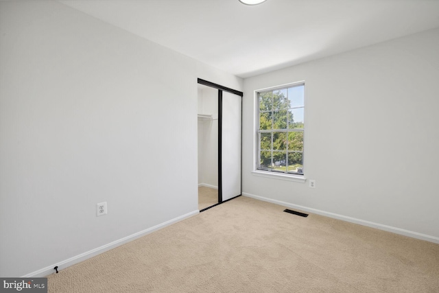 unfurnished bedroom with light carpet and a closet