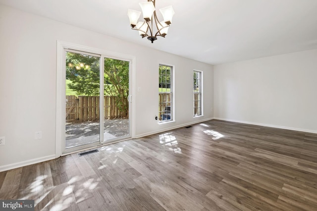 empty room with wood-type flooring and an inviting chandelier