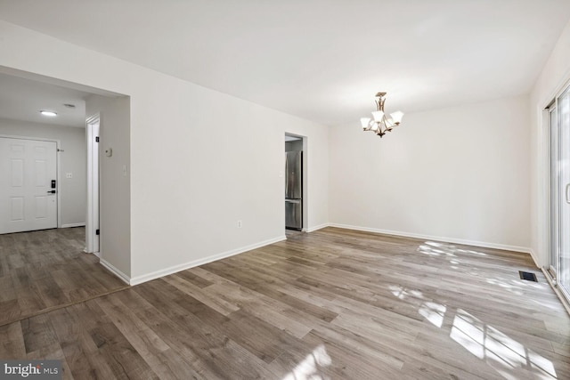 unfurnished room with wood-type flooring and an inviting chandelier