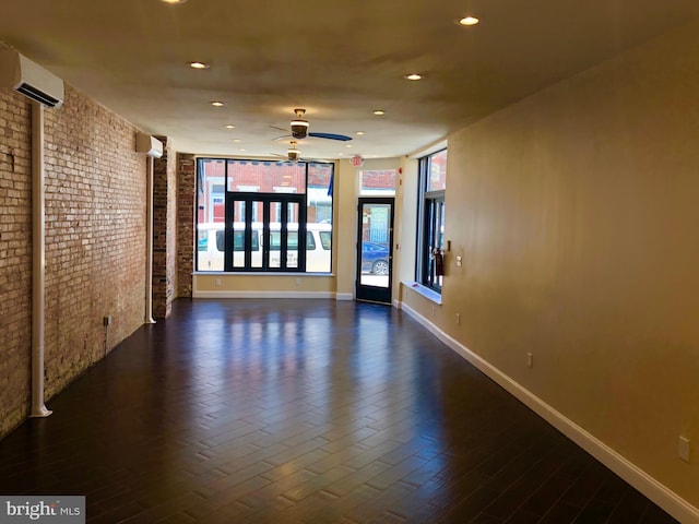 unfurnished room featuring ceiling fan, brick wall, dark hardwood / wood-style flooring, and a wall unit AC