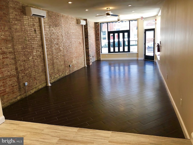 empty room featuring a wall unit AC, ceiling fan, and brick wall