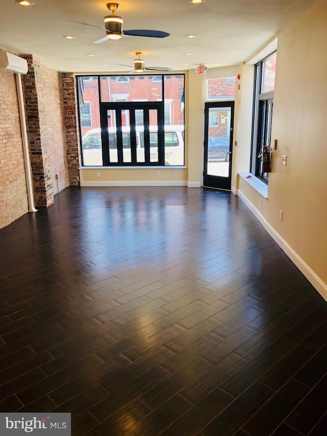 unfurnished room with ceiling fan, a wall mounted AC, dark hardwood / wood-style floors, and brick wall