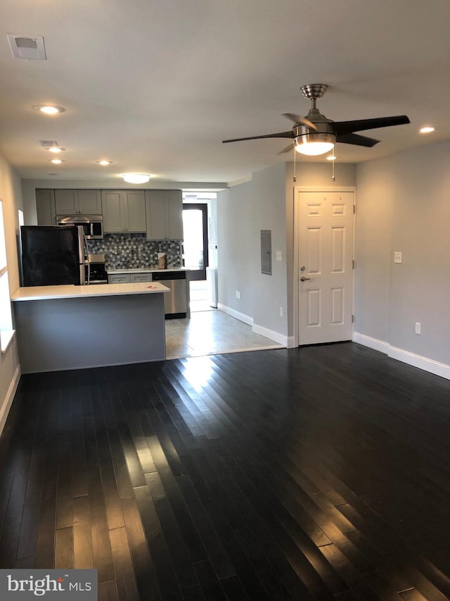 kitchen featuring backsplash, kitchen peninsula, appliances with stainless steel finishes, gray cabinetry, and dark hardwood / wood-style flooring