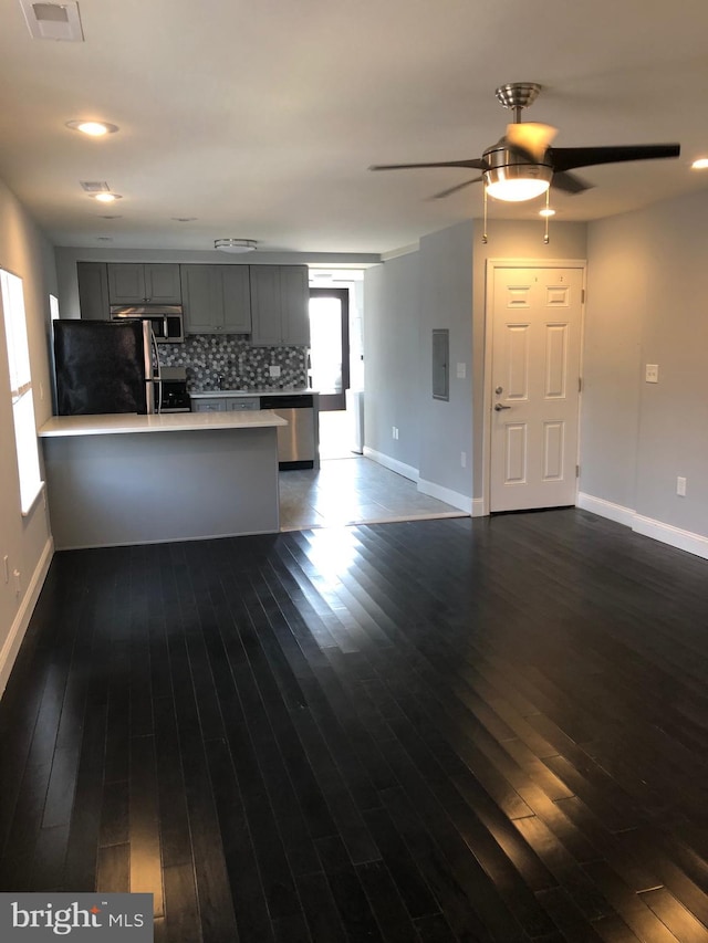 kitchen with kitchen peninsula, gray cabinets, stainless steel appliances, decorative backsplash, and dark wood-type flooring