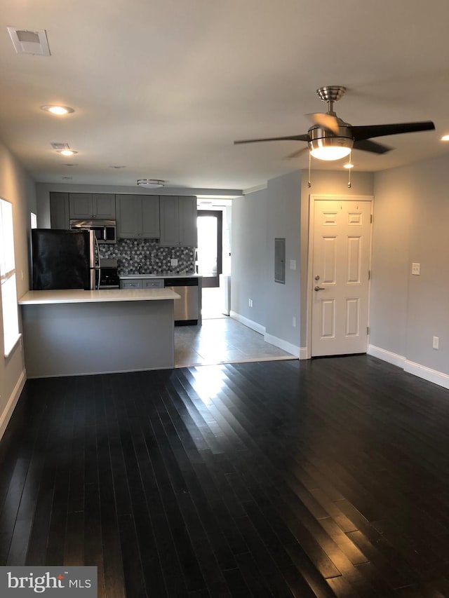 kitchen featuring kitchen peninsula, decorative backsplash, gray cabinetry, stainless steel appliances, and dark hardwood / wood-style flooring