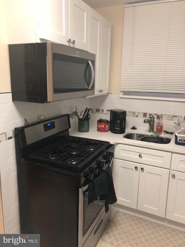 kitchen with backsplash, appliances with stainless steel finishes, sink, and white cabinetry