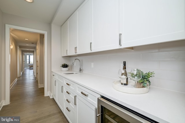 bar with sink, wine cooler, light hardwood / wood-style floors, white cabinets, and decorative backsplash