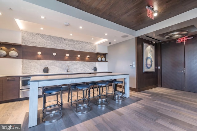 bar with decorative backsplash, wood-type flooring, wooden ceiling, and stainless steel oven