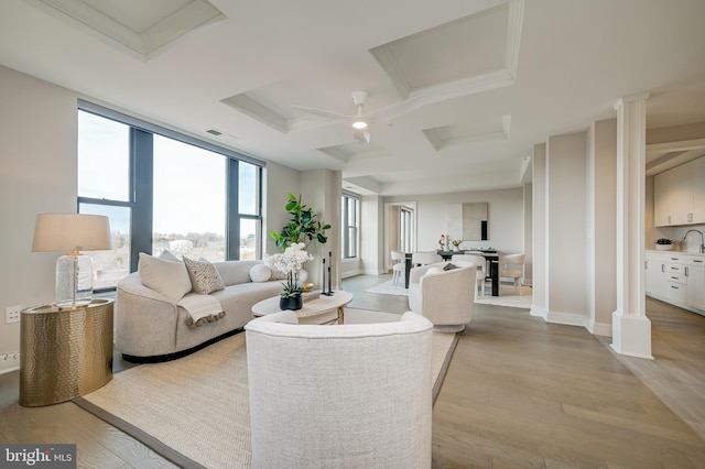 living room with decorative columns, expansive windows, coffered ceiling, and light hardwood / wood-style floors