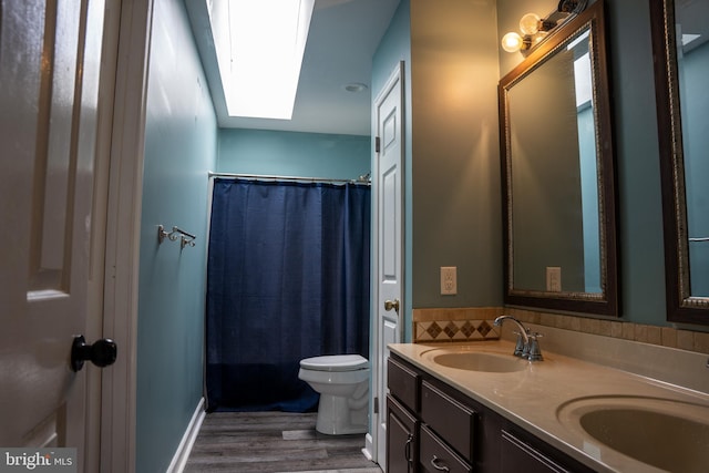 bathroom featuring toilet, vanity, hardwood / wood-style floors, a shower with curtain, and a skylight