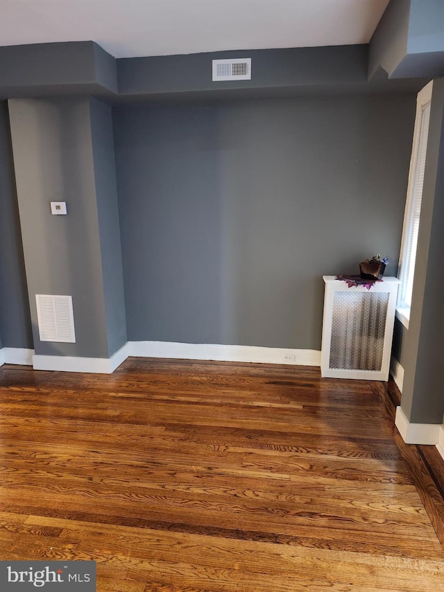 empty room with dark hardwood / wood-style floors and radiator