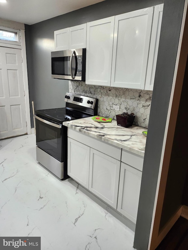 kitchen featuring white cabinets, light stone counters, appliances with stainless steel finishes, and tasteful backsplash