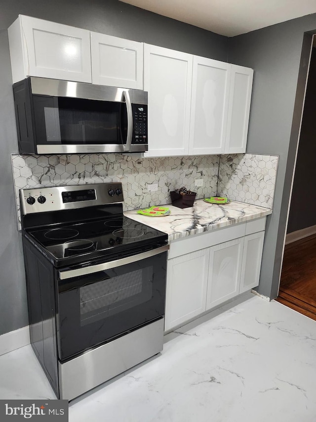 kitchen featuring white cabinets, light stone counters, backsplash, and appliances with stainless steel finishes