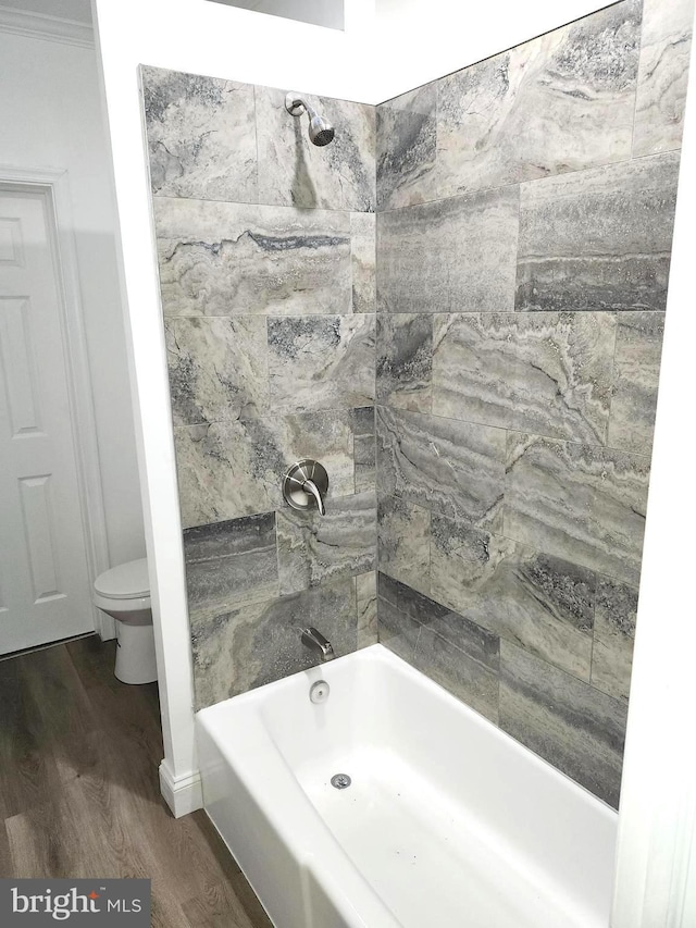 bathroom featuring hardwood / wood-style floors, tiled shower / bath, ornamental molding, and toilet