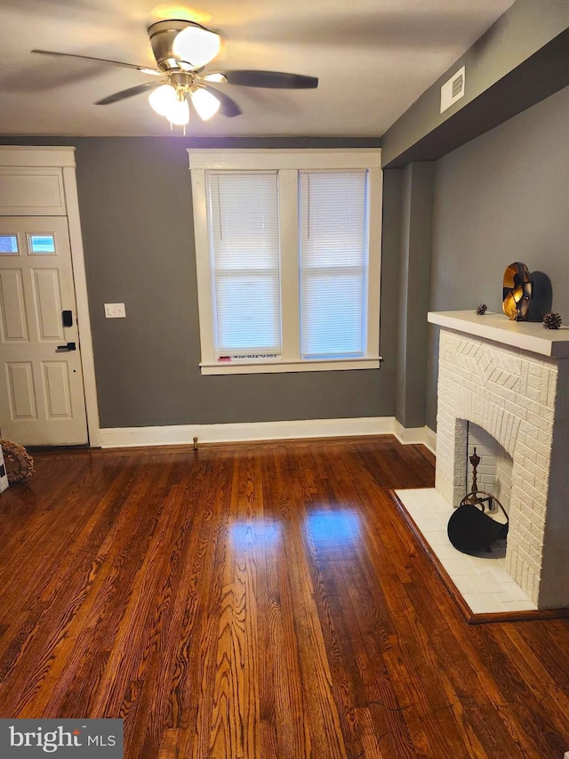 unfurnished living room with ceiling fan, dark wood-type flooring, and a brick fireplace