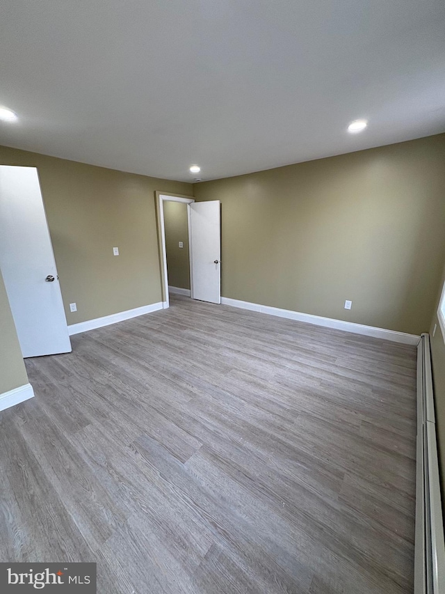 unfurnished room featuring baseboard heating and wood-type flooring